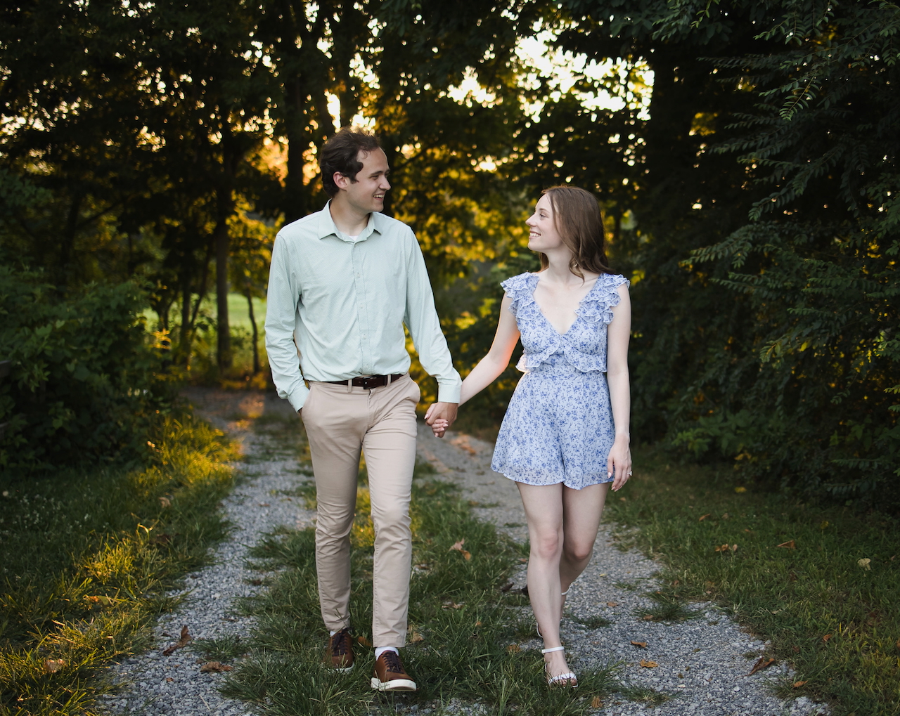 Josh and Jessika holding hands walking along a tree-lined path, smiling at each other