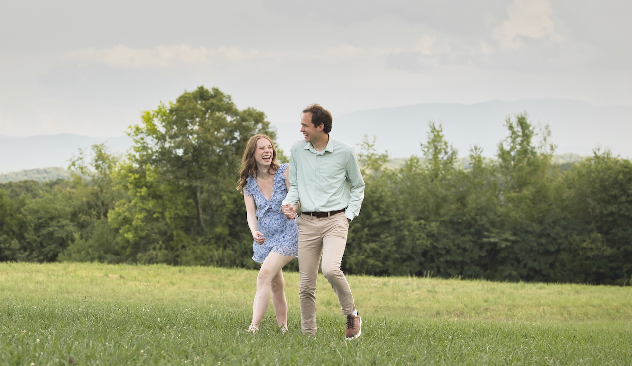 Josh and Jessika holding hands and laughing as they walk through a grassy field