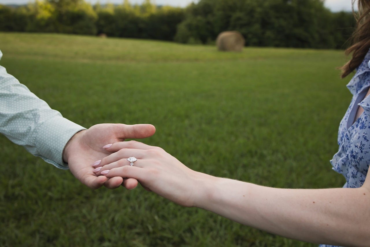 A close-up photo of Josh's hand holding Jessika's hand with the ring shining at the center of the frame